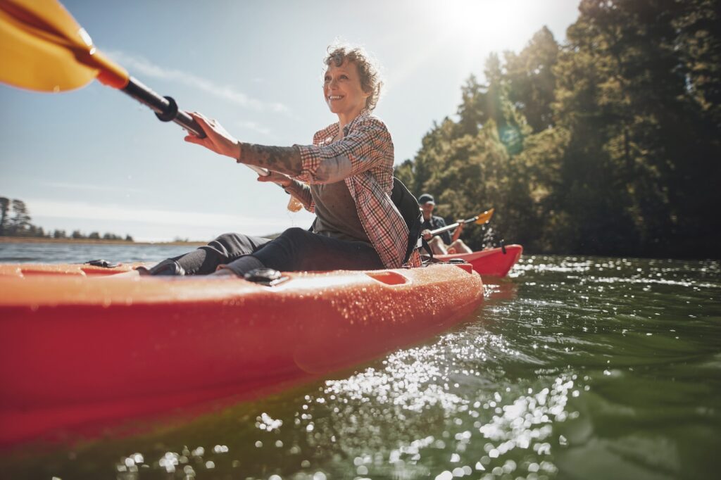 Shot of senior woman canoeing in lake on a summer day. Mature woman paddling a kayak in lake.
